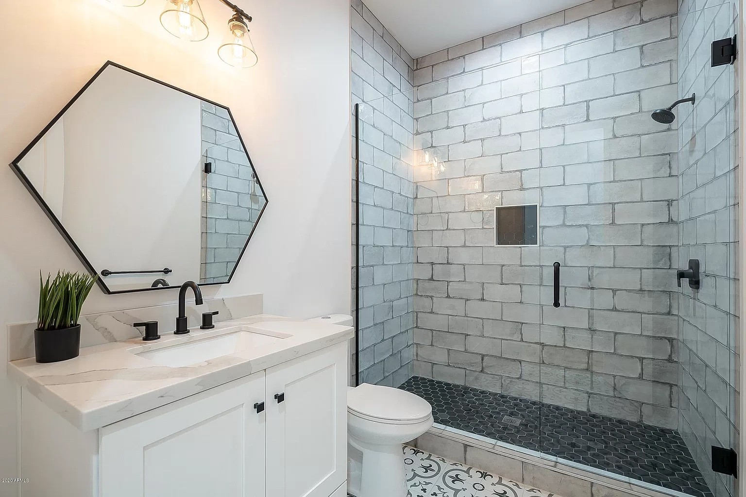 Bathroom with a tiled walk-in shower, hexagon mirror, white vanity and patterned floor tile