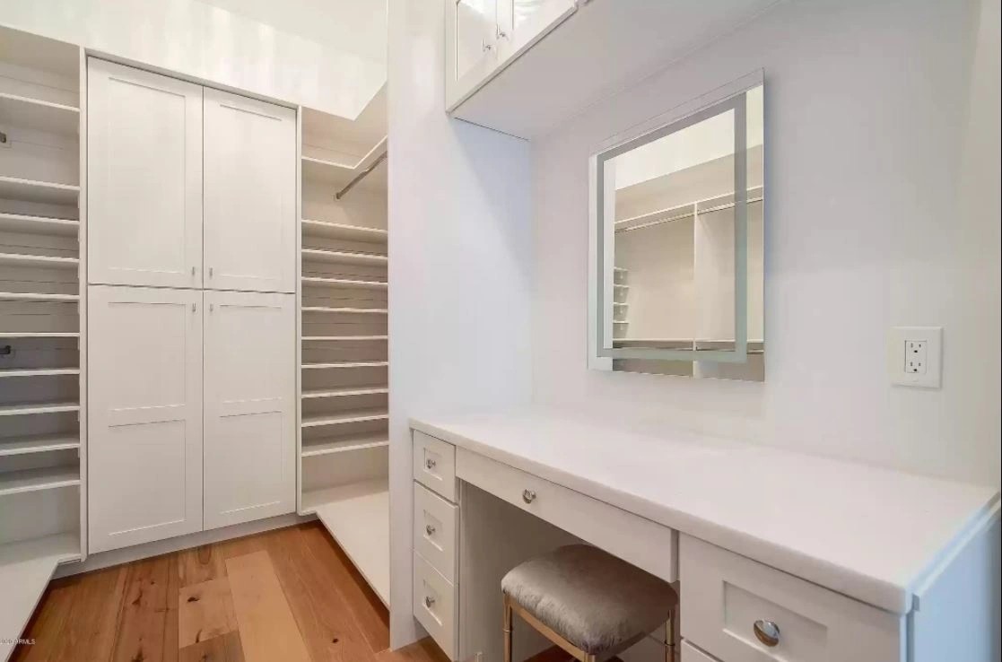 Walk-in closet with white shelving, hanging rails and a built-in vanity with a quartz top and mirror
