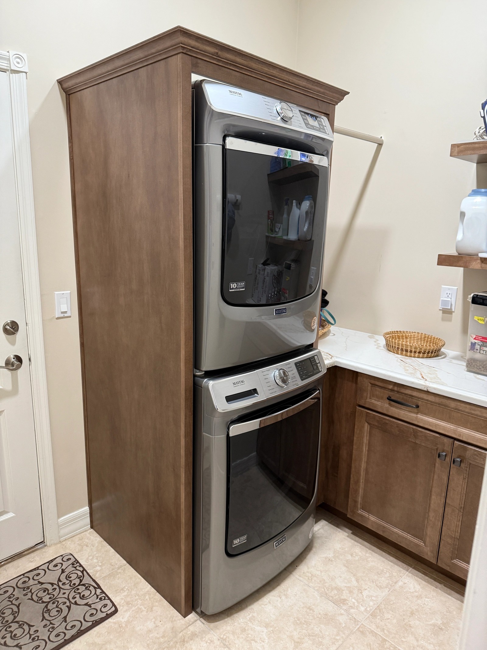 Laundry room with stained maple cabinetry surrounding stacked machines and a quartz folding counter
